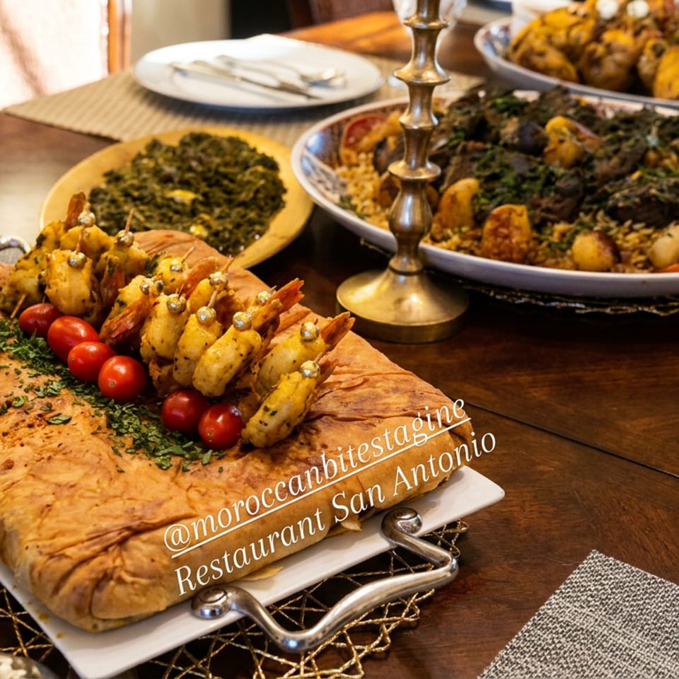 Moroccan feast served on a wooden dining table, featuring flatbread topped with shrimp skewers, cherry tomatoes, couscous, and vegetables.