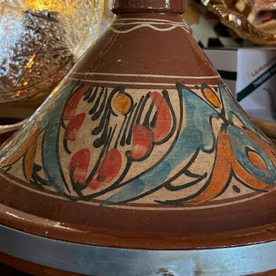 Colorfully painted Moroccan tagine with floral patterns displayed on a metal serving tray among decorative tableware.