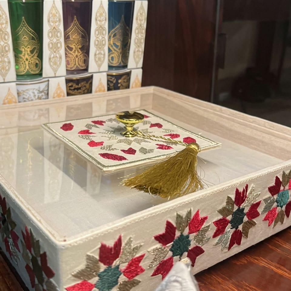 Embroidered decorative box with floral patterns, gold tassel, and ornate patterned containers displayed on a wooden table.